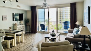 A spacious living area with a balcony, a dining table, and a sofa. - Gorgeous Sunset Condo at One of the Most Beautiful Pool Resorts on the Beach!  (Panama City Beach)
