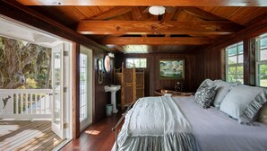 A wooden cabin bedroom with a bed, a window, a painting, and a view of the outdoors.