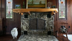 A stone fireplace with a wooden mantel, framed artwork above, and a rustic wooden floor.