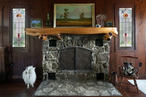 A stone fireplace with a wooden mantel, framed artwork above, and a rustic wooden floor.