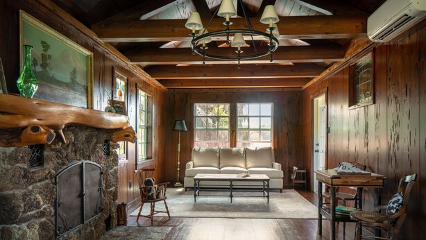 A cozy room with a stone fireplace, wooden walls, a sofa, and a chandelier.