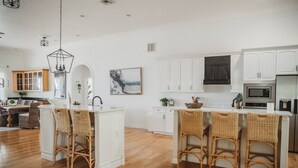 Cozinha moderna com armários brancos, uma ilha central com banquetas e um lustre.