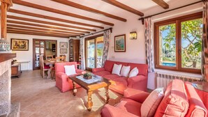A cozy living room with a wooden ceiling, a red sofa, a coffee table, and a view of the outdoors through large windows. - L'Olivar Cánaves - Four Bedroom Villa, Sleeps 8 (Mallorca)