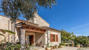 A stone building with a tiled roof, a wooden door, and a small porch with potted plants. - L'Olivar Cánaves - Four Bedroom Villa, Sleeps 8 (Mallorca)