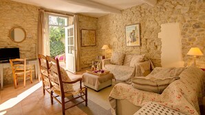 A cozy room with stone walls, a wooden chair, a sofa, a television, and a table with a tray of items.