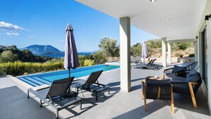 A modern outdoor pool area with lounge chairs and umbrellas, overlooking a scenic landscape with mountains and a clear sky. - Kristi - Three Bedroom Villa, Sleeps 6 (Spartochori)