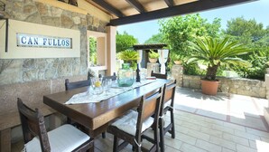 An outdoor patio with a stone wall, a wooden table set with glasses and a pitcher, and a sign that reads "CAN FULLOS".