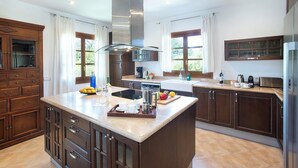 A modern kitchen with a central island, dark wooden cabinets, and a stainless steel refrigerator. - C'an Pontarro - Five Bedroom Villa, Sleeps 10 (Mallorca)