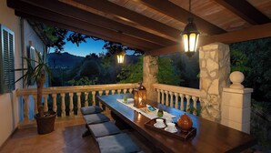 An outdoor dining area with a long wooden table, cushioned benches, and a lantern. - C'an Pontarro - Five Bedroom Villa, Sleeps 10 (Mallorca)