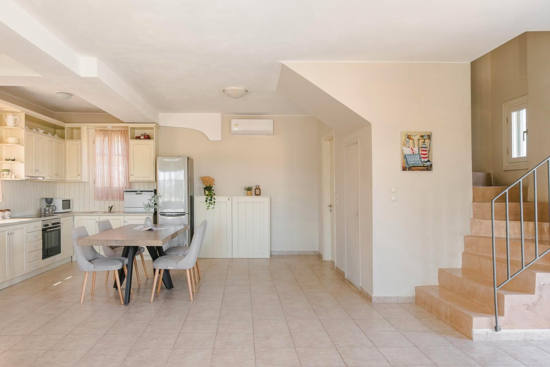 Een moderne keuken met witte kasten, een eethoek met een houten tafel en stoelen, en een trap die naar een hoger niveau leidt.