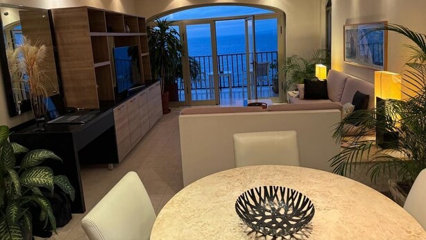 A modern living room with a balcony overlooking the sea, a dining area with a round table, and a kitchen with wooden cabinets. - BEAUTIFUL VIEWS ON PLAYAS GEMELAS BEACH (PUERTO VALLARTA)