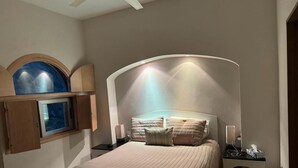 A bedroom with a large bed, a headboard with integrated lighting, a bedside table with a lamp, a small shelf, and a window with a view. - BEAUTIFUL VIEWS ON PLAYAS GEMELAS BEACH (PUERTO VALLARTA)