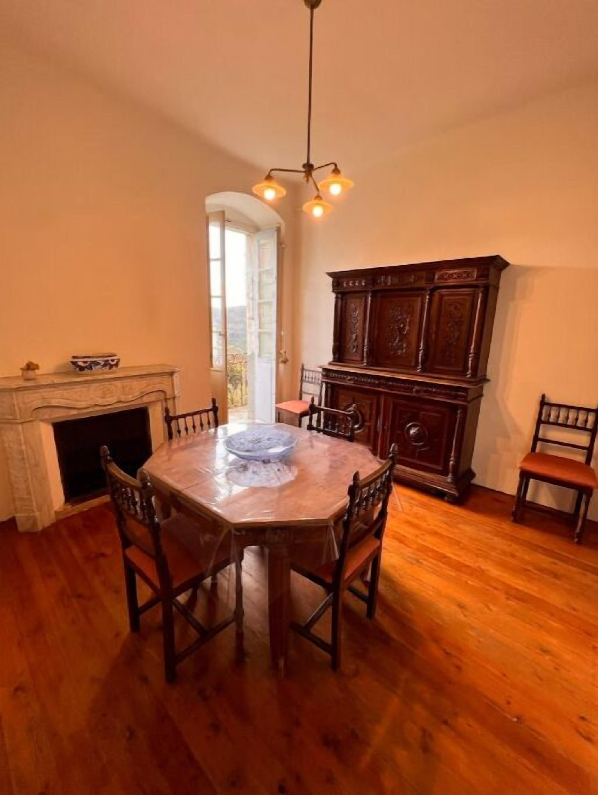 Une salle à manger avec une table ronde en bois, six chaises, un lustre, une cheminée et un grand buffet en bois.