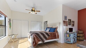 Ein Schlafzimmer mit Bett, Deckenventilator, Fenster und einer Wand mit Bildern.