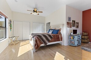A bedroom with a bed, a ceiling fan, a window, and a wall with pictures.