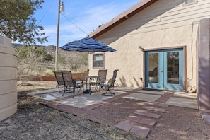Un patio al aire libre con una mesa, sillas, un paraguas a rayas y una puerta con ventanal.