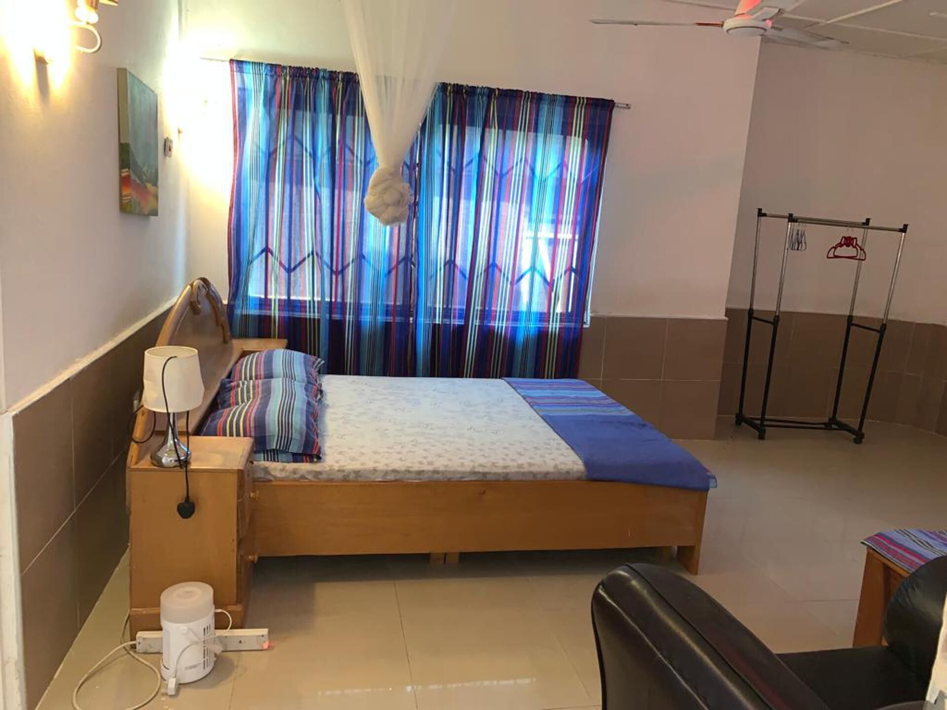 Quarto com uma cama, mesa de cabeceira com abajur, régua de tomadas e uma cadeira.