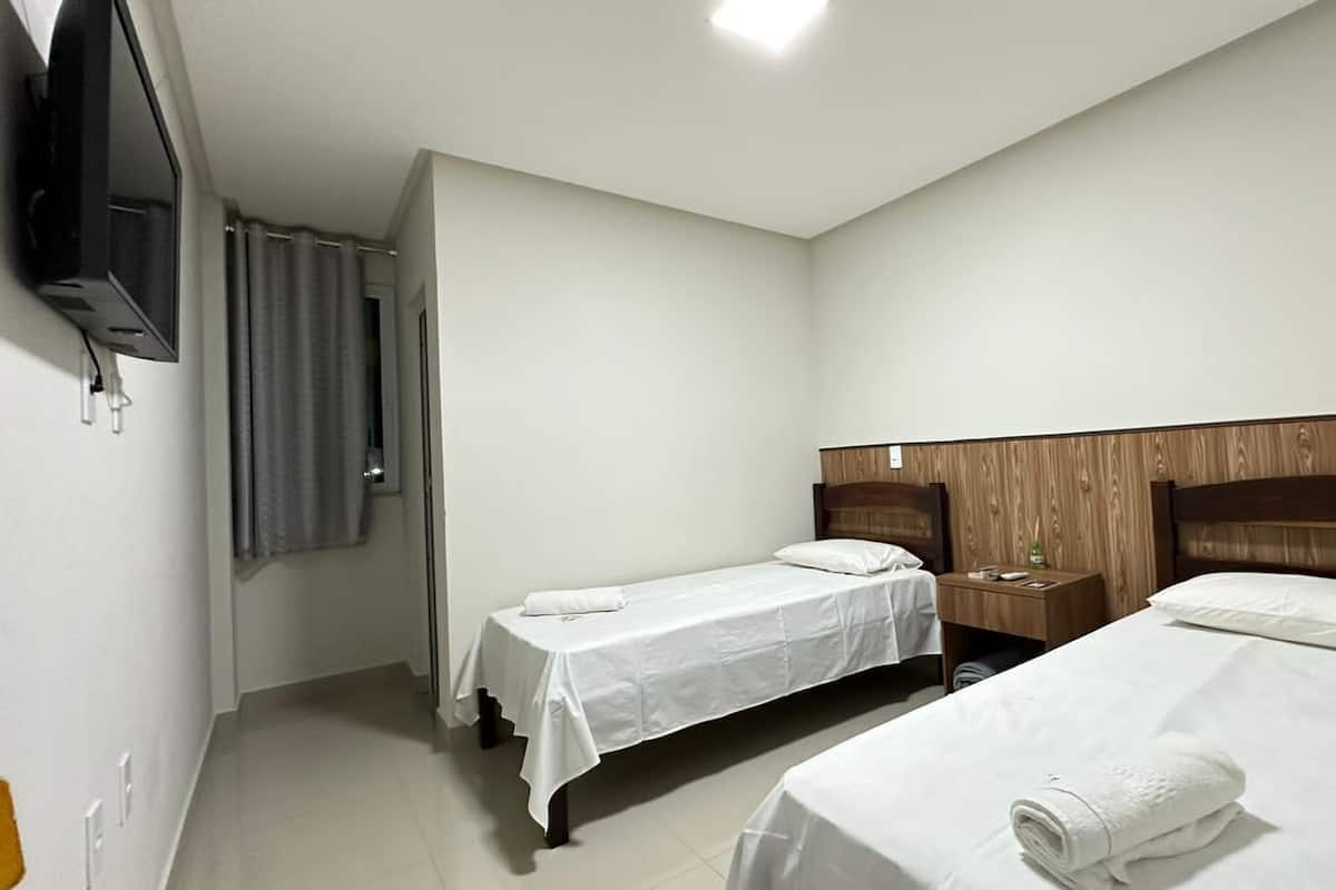 A hotel room with two single beds, a wooden headboard, a nightstand, and a flat-screen TV mounted on the wall.