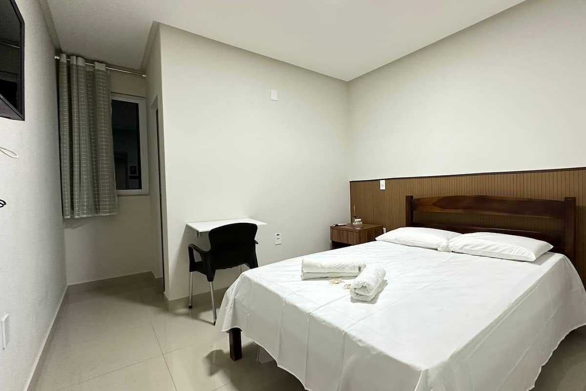 A hotel room with a bed, a desk, a chair, and a nightstand.