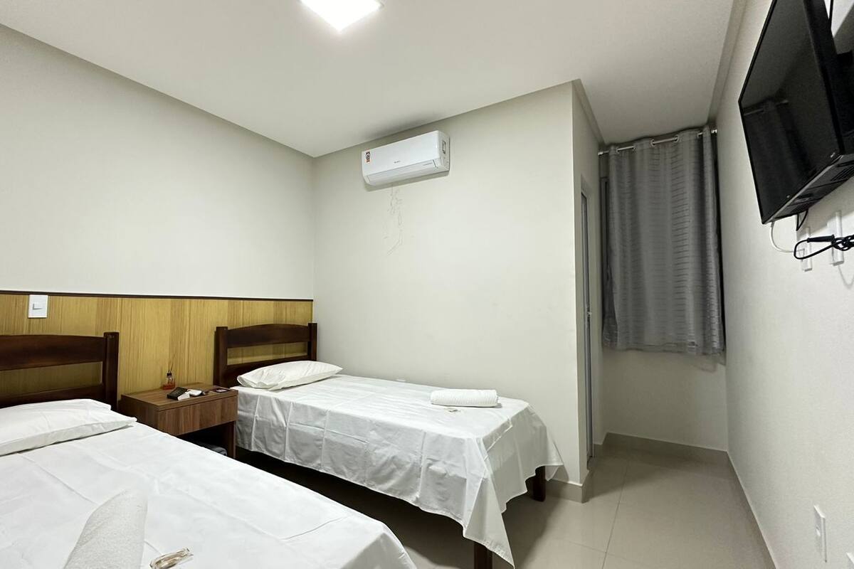 A hotel room with two single beds, a wooden headboard, a nightstand, a TV, and an air conditioning unit.
