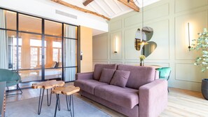 A modern living room with a sofa, wooden tables, and a view through a glass door.