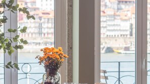 A window with a view of a river and buildings, a vase with flowers, and a plant on the window sill. - Riverside Oasis by LovelyStay (Vila Nova de Gaia)