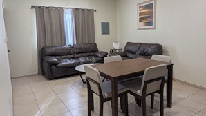 A living room with a brown leather sofa, a wooden dining table with four chairs, and a small side table. - Cómodo Departamento Y Para Cuatro Personas, Cerca del Aeropuerto de Loreto (Loreto)