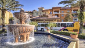 Una fuente con chorros de agua, un autobús y un edificio con balcones y tejado de tejas.