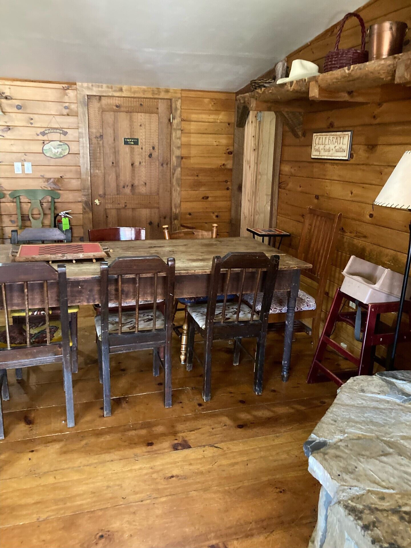A rustic wooden dining area with a large table and chairs, a wooden door, and a shelf with various items.