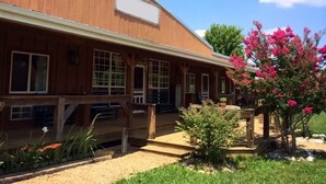 A wooden building with a covered porch and a garden with pink flowers.