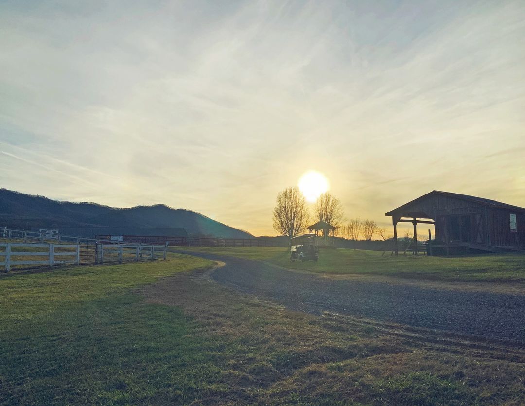 A rural landscape with a dirt road, a barn, and a gazebo under a clear sky.