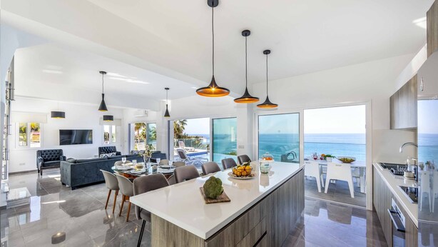 A modern kitchen with a large island, a dining area with chairs, and a view of the ocean.