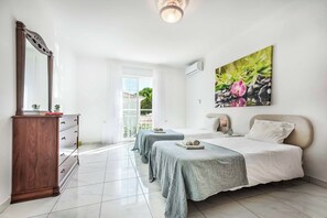A hotel room with two beds, a wooden dresser, a large window, and a painting of flowers.