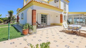Ein zweistöckiges Gebäude mit einer gefliesten Terrasse, einem Essbereich mit Tisch und Stühlen sowie einem kleinen Garten mit Blumentöpfen.
