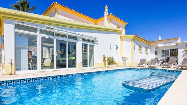 Ein Schwimmbecken mit einer schwimmenden Plattform, einer überdachten Terrasse und einem Gebäude mit großen Glasfenstern.