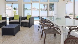 Eine sonnendurchflutete Terrassenfläche mit Korbmöbeln, einem Glastisch und Blick auf Pool und Gebäude im Hintergrund.