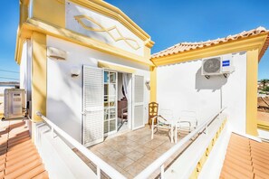 A white building with a yellow facade, a balcony with white railings, and a tiled floor.