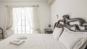 Ein ordentlich bezogenes Bett mit weißen Leinen und Kissen, ein hölzernes Kopfteil und ein Fenster mit Vorhängen.