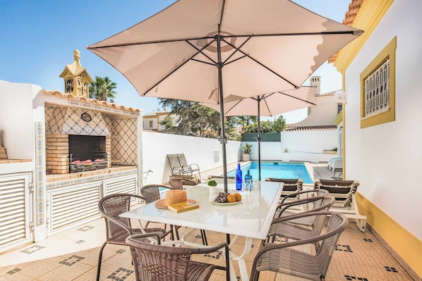 An outdoor patio with a barbecue grill, a pool, and wicker furniture.