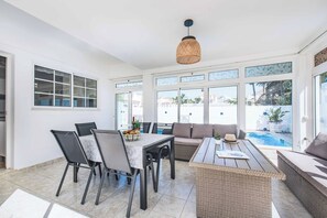 A sunlit patio with a dining table, chairs, a sofa, and a pool view.