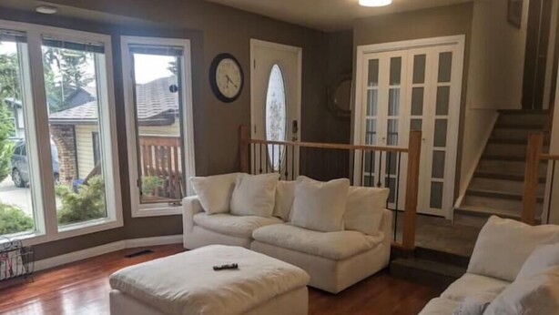 A living room with a white sofa, a matching ottoman, and a wooden staircase.