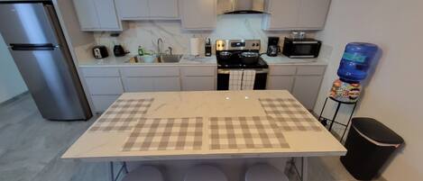 A modern kitchen with a central island, bar stools, stainless steel appliances, and a water dispenser.