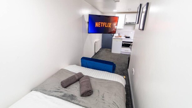 Habitación de hotel con cama, escritorio, kitchenette y televisión mostrando el logo de Netflix.