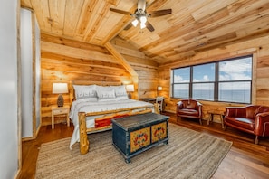 A wooden cabin bedroom with a bed, two chairs, a small table, and a ceiling fan.