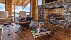 Una habitación acogedora con chimenea de piedra, una mesa de madera con una vela, un cuenco de piñas y un libro.