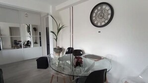 A modern dining area with a glass table and black chairs, a decorative clock on the wall, and a plant in the corner.