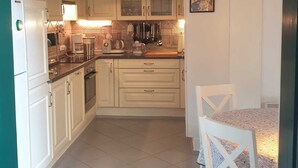 Una cocina compacta con armarios blancos, un refrigerador, un ventilador de techo y una zona de comedor con una mesa y sillas.
