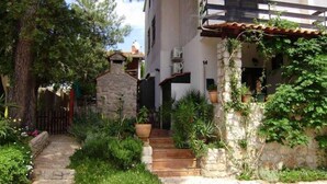 Una escalera de piedra conduce a un edificio blanco de teja, rodeado de abundante vegetación y macetas con plantas.