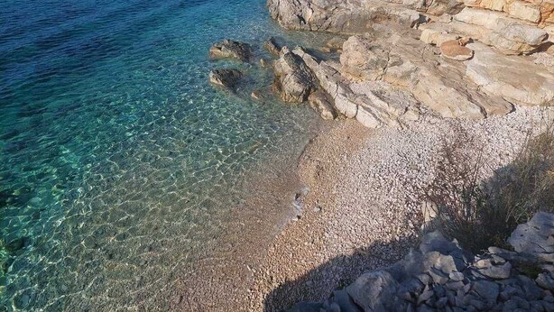 Paisaje costero con agua cristalina, costa rocosa y playa de guijarros.