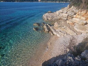 A coastal landscape with clear water, rocky shoreline, and a pebble beach.